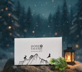 National Park gift voucher in the snow next to a lantern with a winter forest background | © Ferienregion Nationalpark Hohe Tauern 
