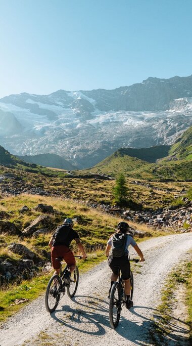 Two mountain bikers riding on a gravel road towards a glacier. | © Mathäus Gartner