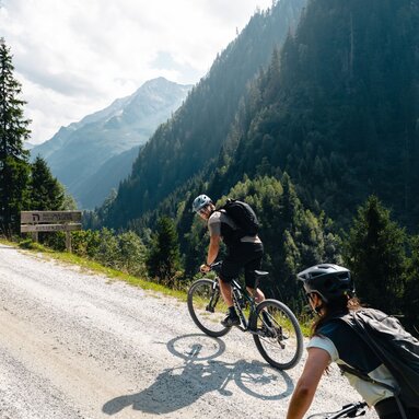 Zwei Mountainbiker fahren bergauf auf Schotterstraße im Tal. | © Mathäus Gartner