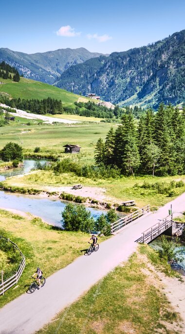 Radfahrer überqueren Brücke in grüner Tallandschaft. | © Daniel KOgler