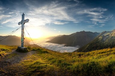 Gipfelkreuz auf Bergwiese mit Sonnenaufgang und Nebelmeer. | © Ferienregion Nationalpark Hohe Tauern / Florian Kreidl-Glueck
