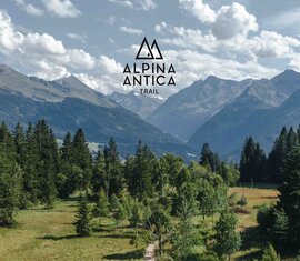 Alpina Antica Trail logo against a mountain panorama with forests and meadows. | © Alpina Antica Trail