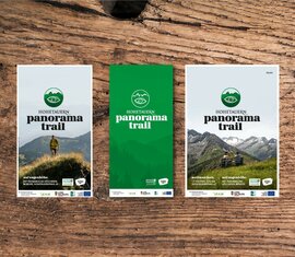 Three brochures of the Hohe Tauern Panorama Trail on a rustic wooden table. | © Vacation region Hohe Tauern National Park